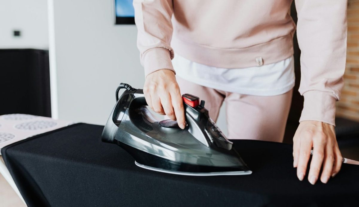 Person ironing black fabric on an ironing board with a modern steam iron
