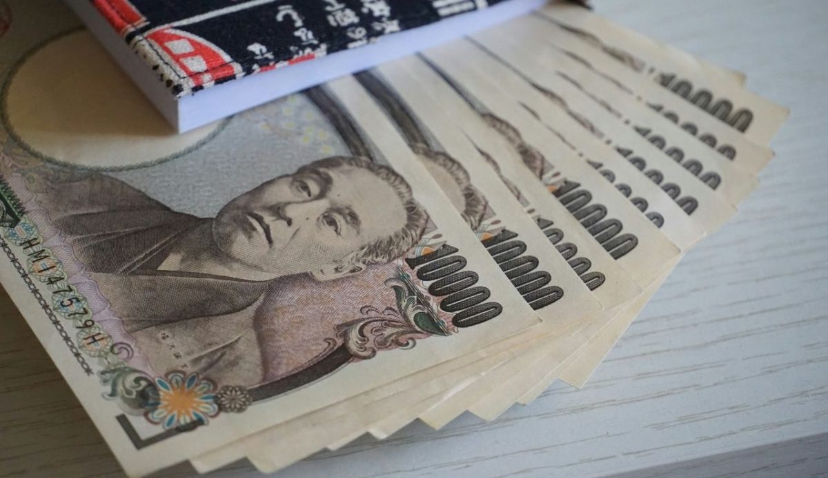 Stack of Japanese 10000 yen banknotes partially covered by a patterned notebook
