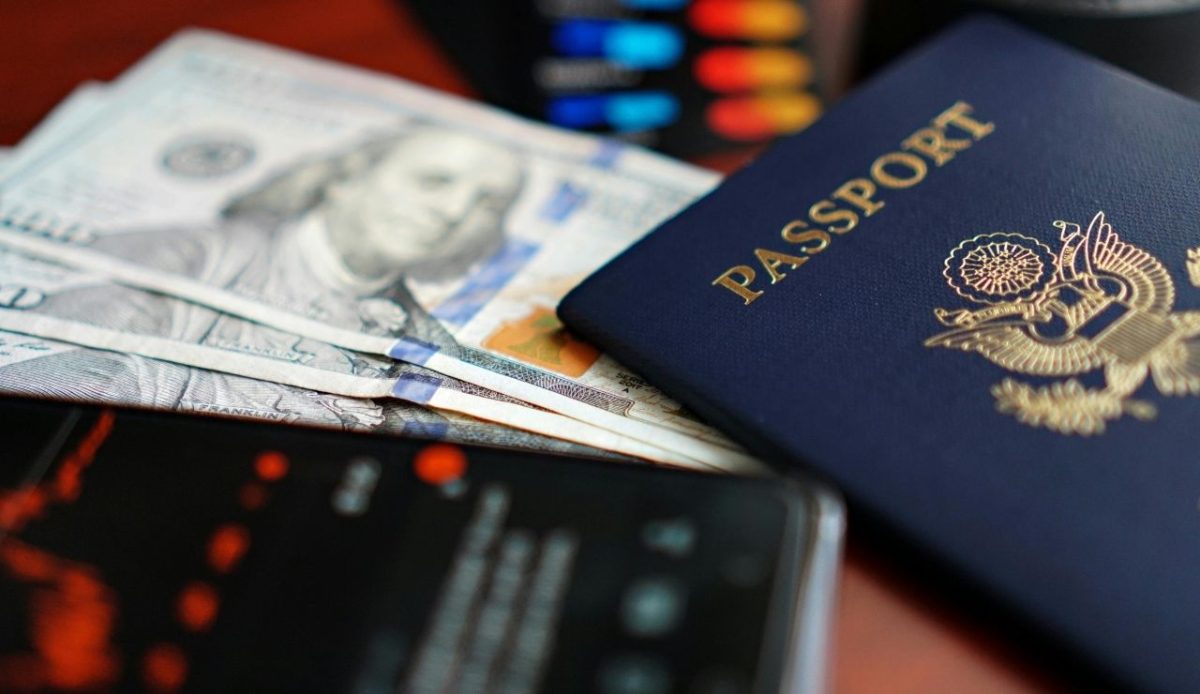 U.S. passport placed on top of hundred dollar bills with a smartphone nearby
