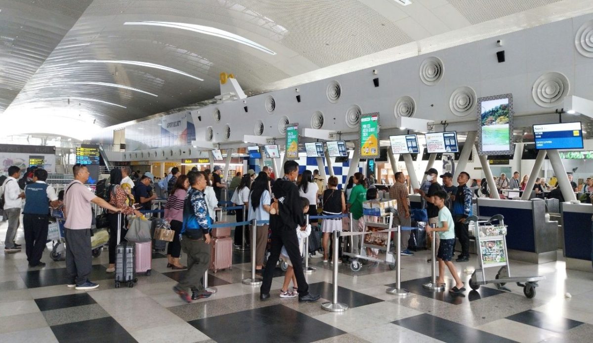 Passengers standing in line at airport check in counters with luggage and trolleys
