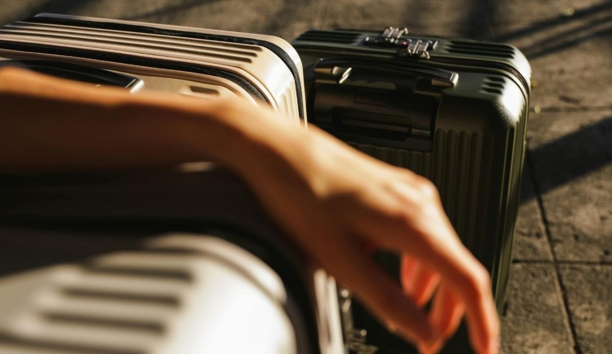 Traveler’s hand resting near hard shell suitcases placed outdoors in sunlight
