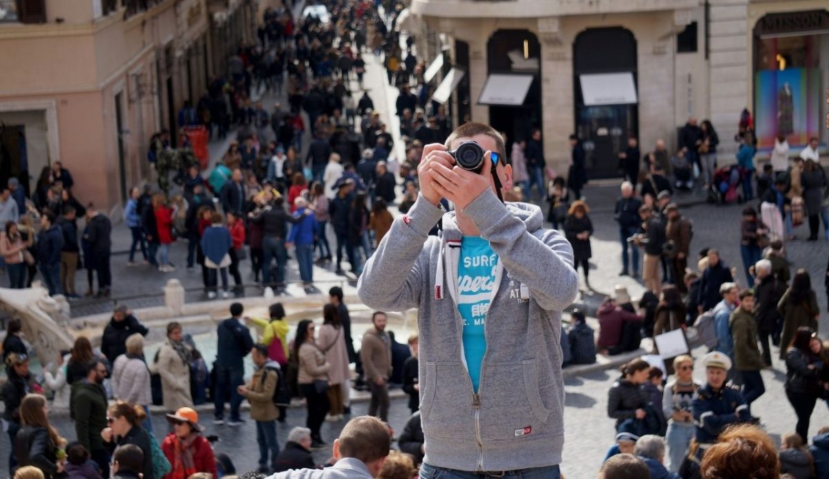 9 Travel Habits Quietly Changing How People Explore 4 Tourist taking a photo with a camera in a crowded city square