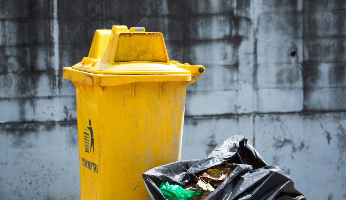 Yellow outdoor trash bin beside a black garbage bag filled with waste
