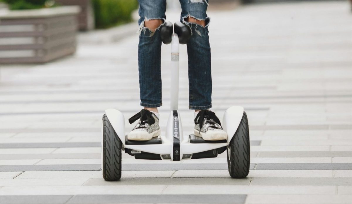 Person riding a white hoverboard with black sneakers on a paved pathway
