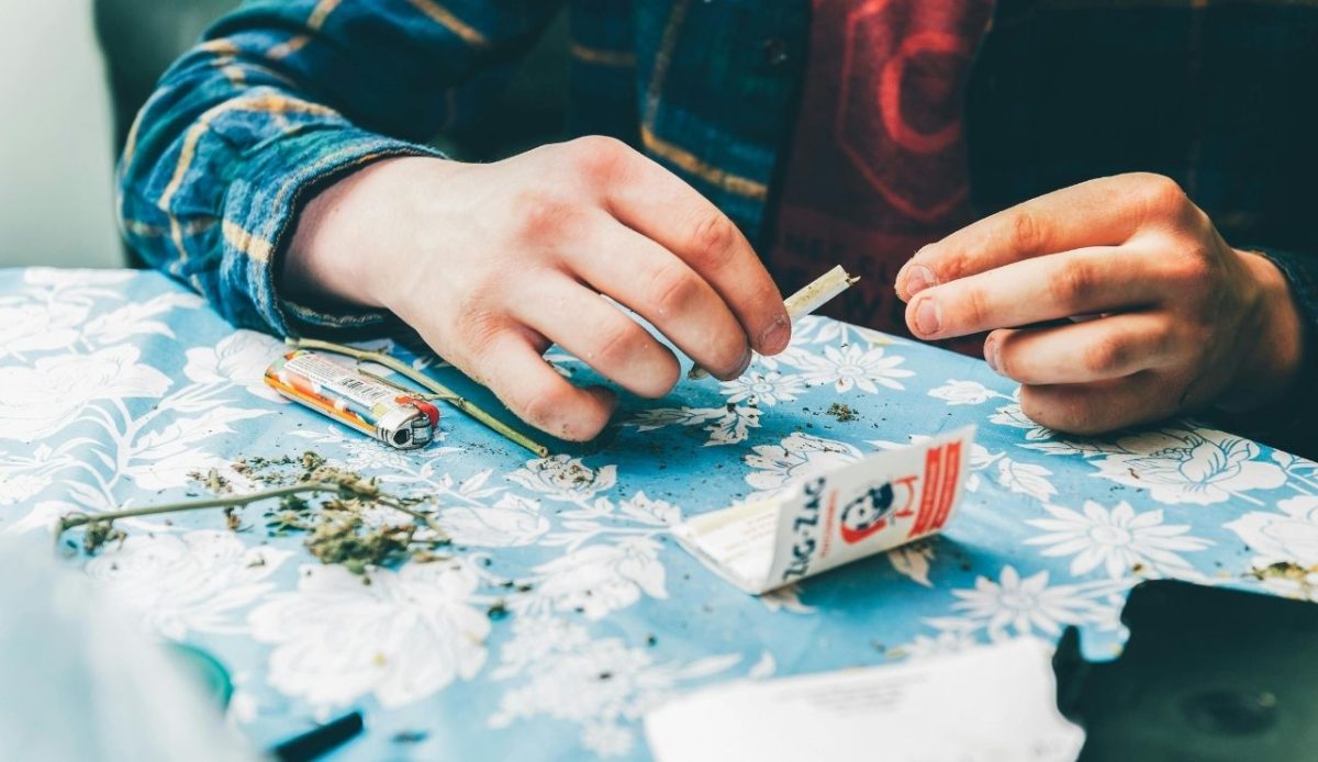 Person rolling a joint with cannabis and rolling papers on a table
