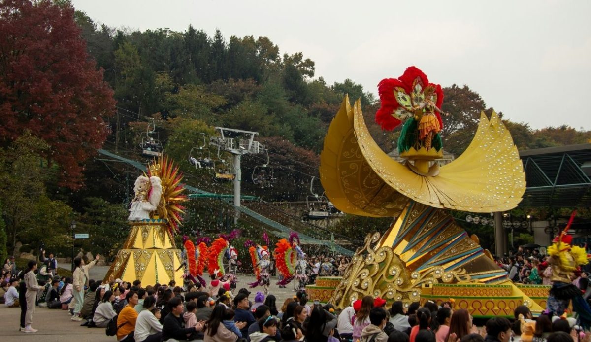 Colorful parade floats with performers in vibrant costumes entertaining a large seated crowd outdoors
