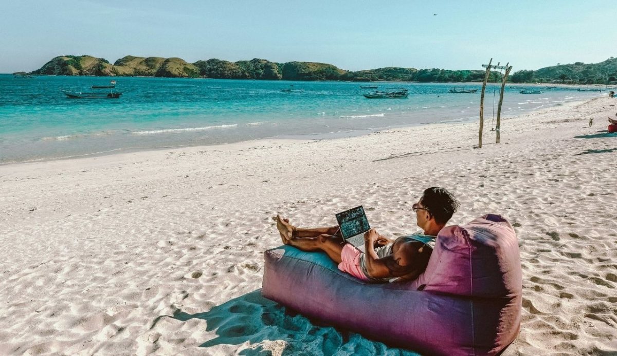 9 Travel Habits Quietly Changing How People Explore 5 Man relaxing on a bean bag at the beach while using a laptop