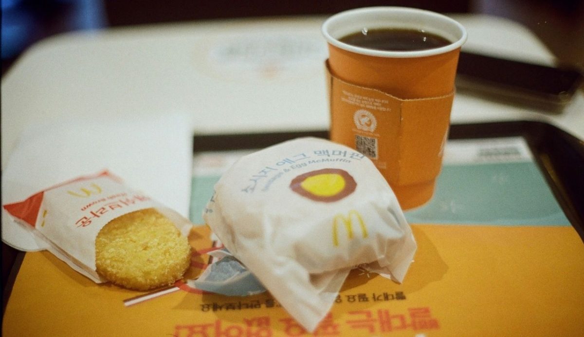 McDonald’s breakfast meal with hash brown, wrapped sausage and egg McMuffin, and a cup of hot coffee on a tray
