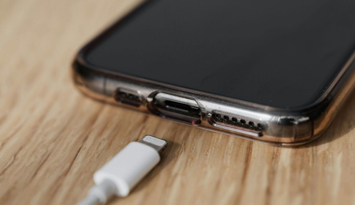 Close up of a smartphone with a transparent case placed near a white charging cable on a wooden surface
