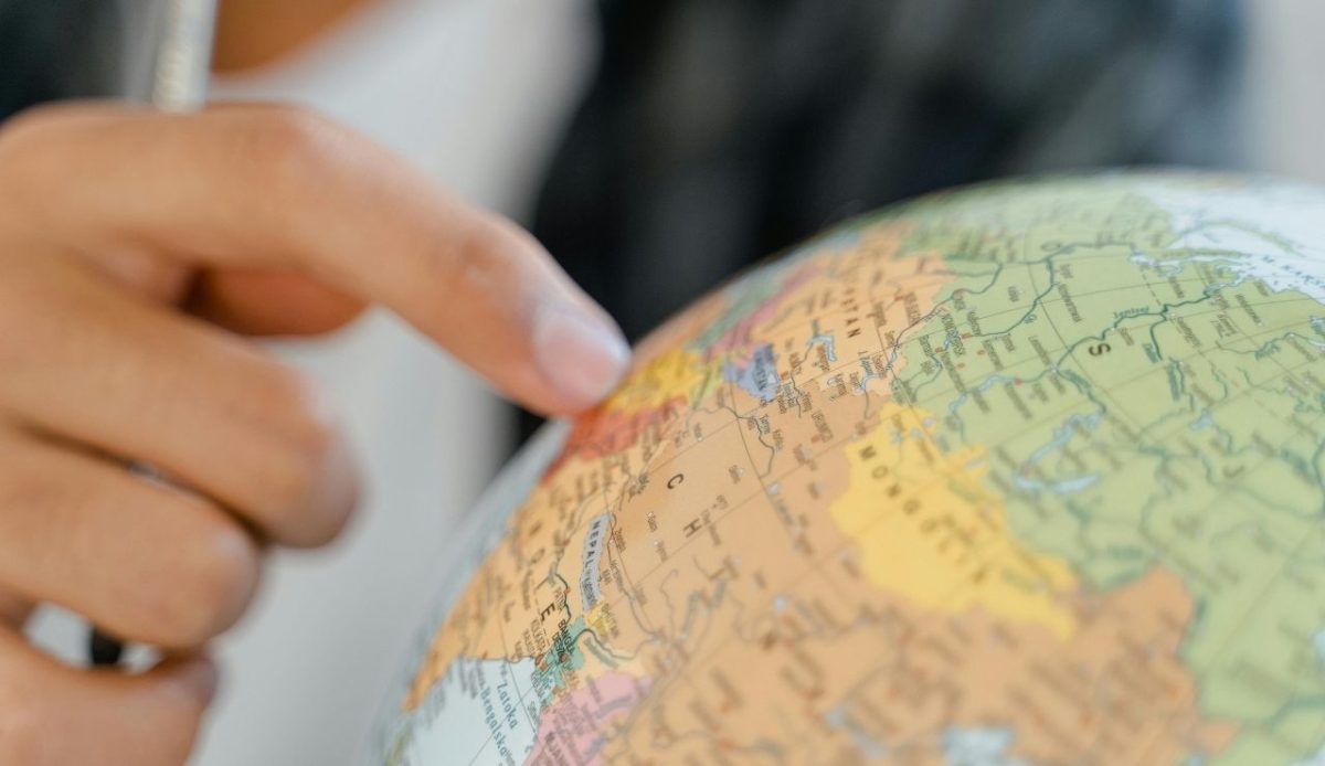Close-up of a hand pointing at a location on a globe map
