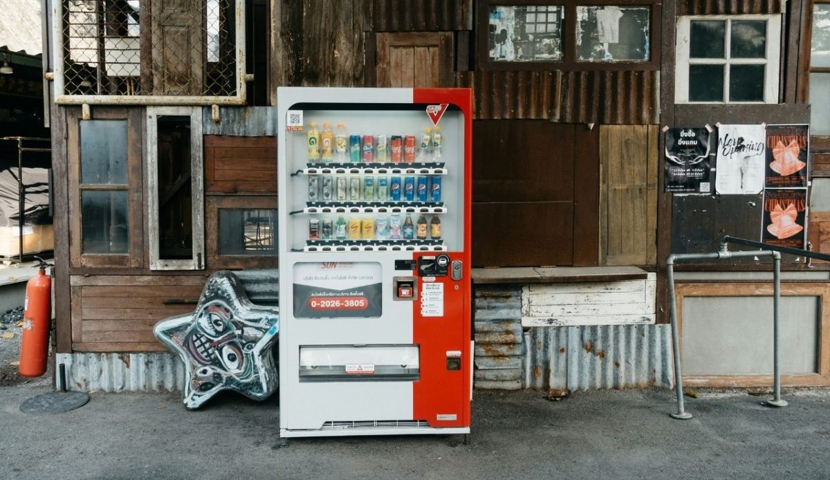 Drink vending machine placed in front of an old wooden building with posters on the wall
