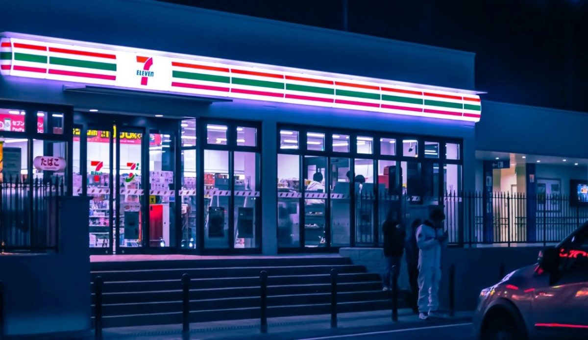 7-Eleven convenience store lit up at night with people standing outside
