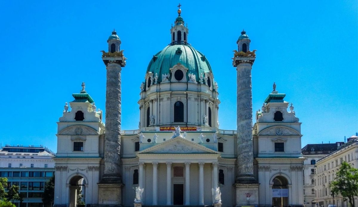 St. Charles Church (Karlskirche) in Vienna with its green dome and twin columns against a clear blue sky
