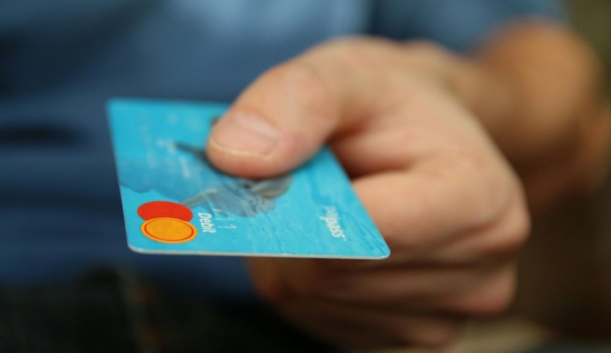 A close-up of a person holding out a blue debit card with a red and orange chip logo visible.
