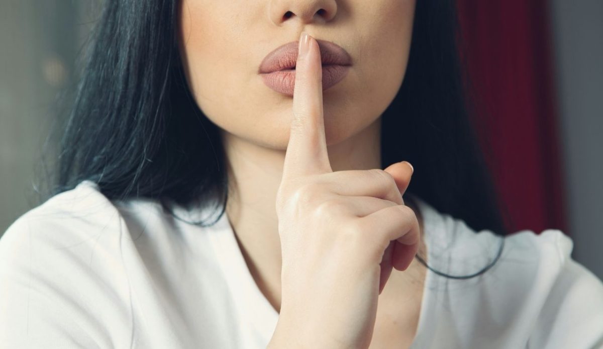 Woman holding finger to lips making a shushing gesture for silence
