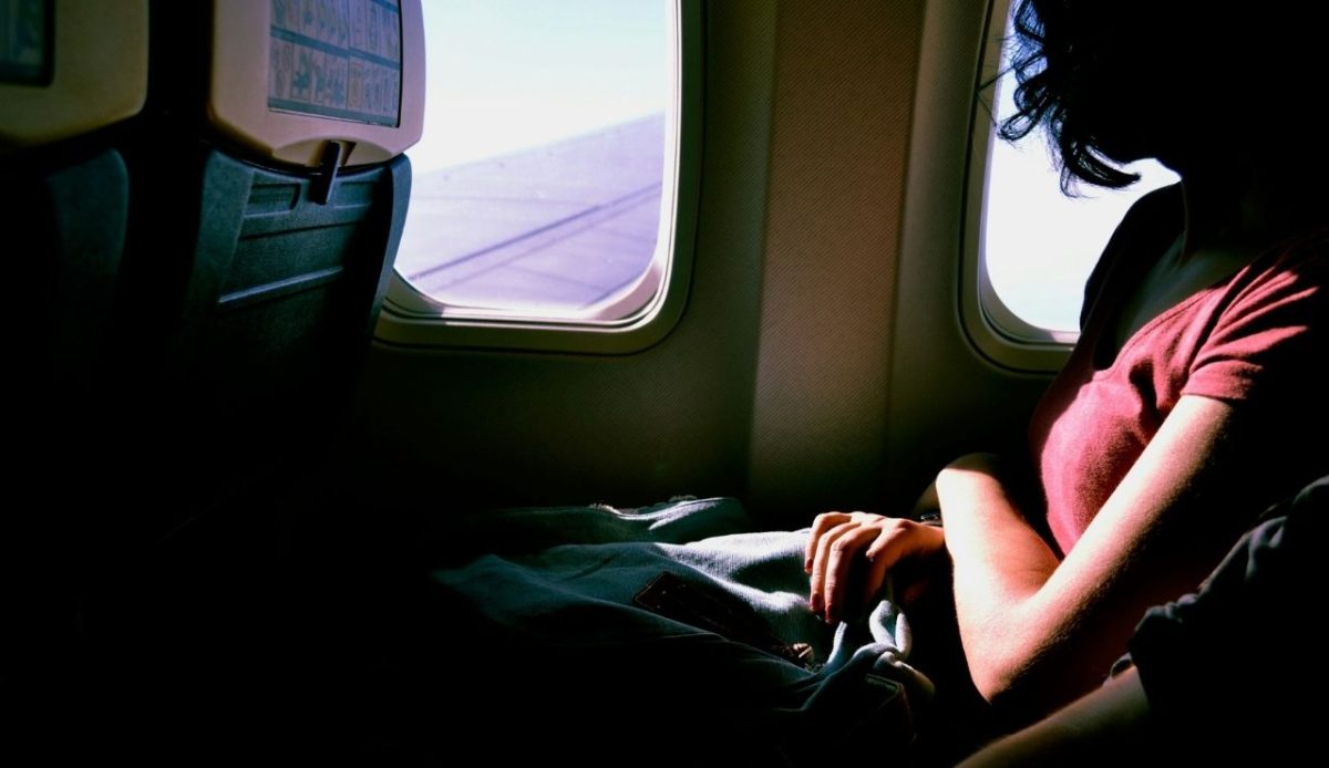 Passenger sitting by an airplane window with sunlight shining through and wing visible outside
