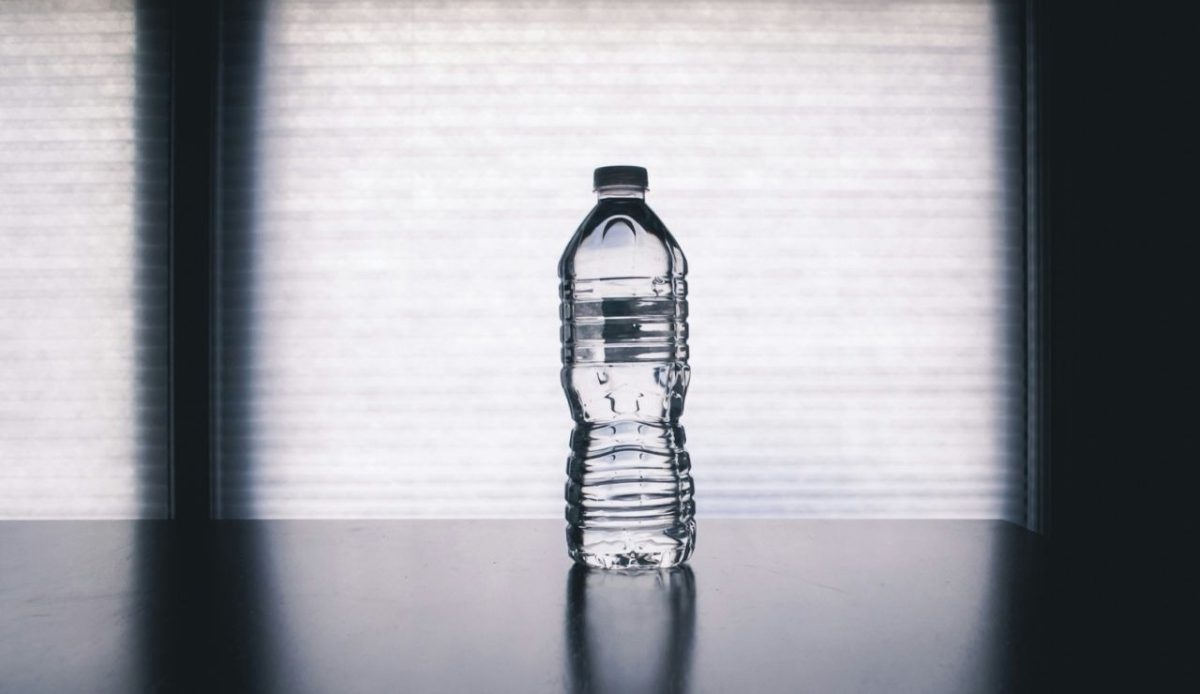 Plastic water bottle filled with water placed on a reflective surface against a bright window background
