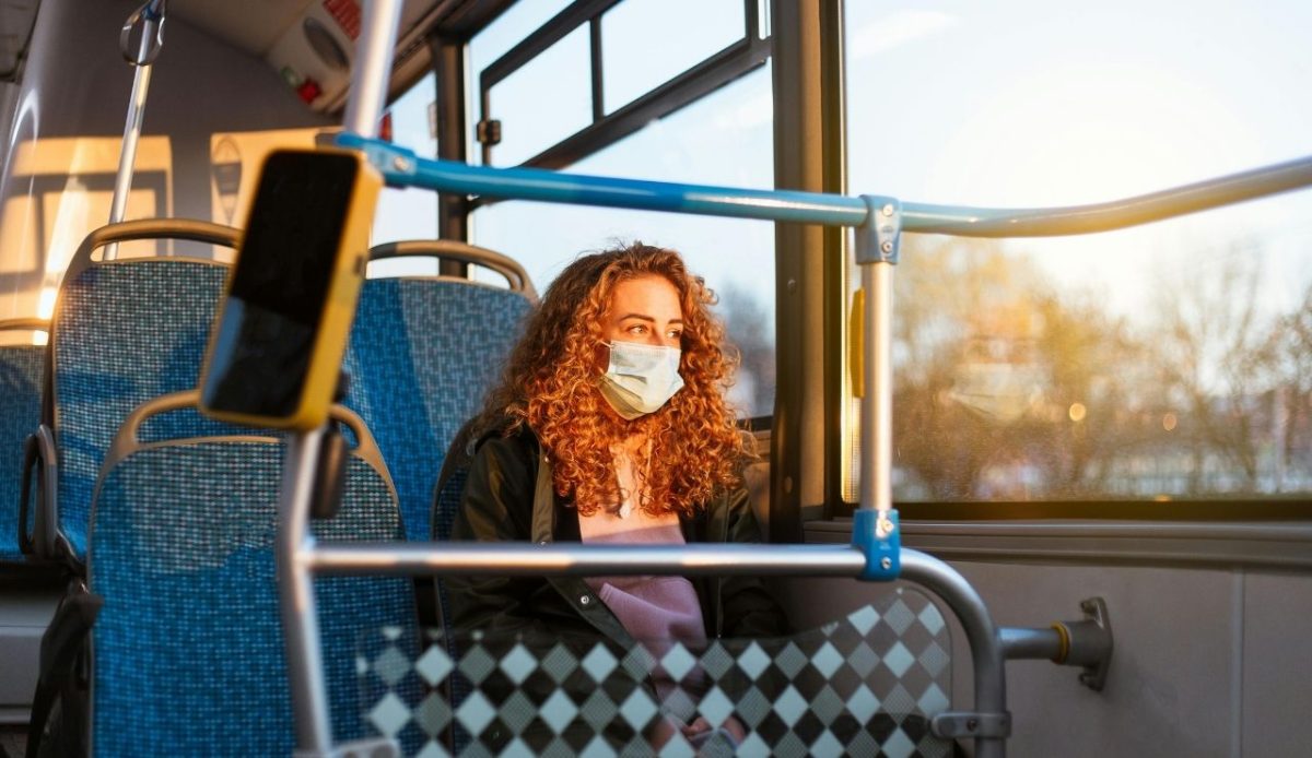 Woman wearing mask sitting near window on a bus