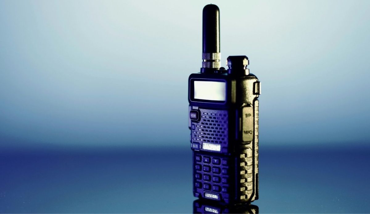 Close up of a handheld walkie talkie radio with antenna on a reflective surface
