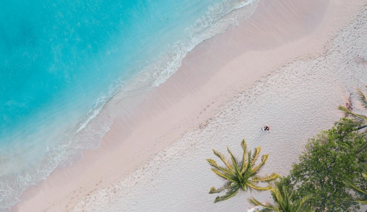 9 Travel Habits Quietly Changing How People Explore 6 Aerial view of a tropical beach with turquoise water, white sand, and palm trees
