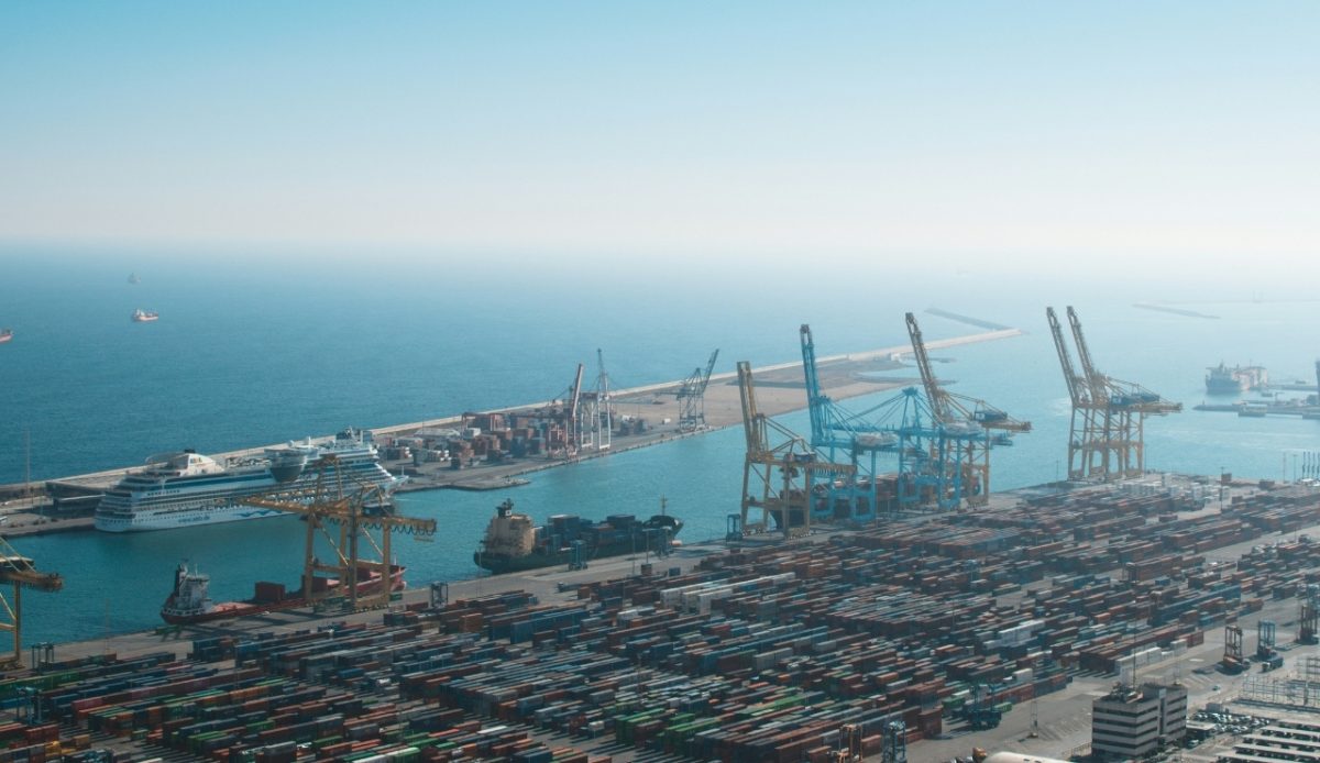 Aerial view of the port with cargo containers and a cruise ship docked, likely at the Port of Barcelona, Spain 