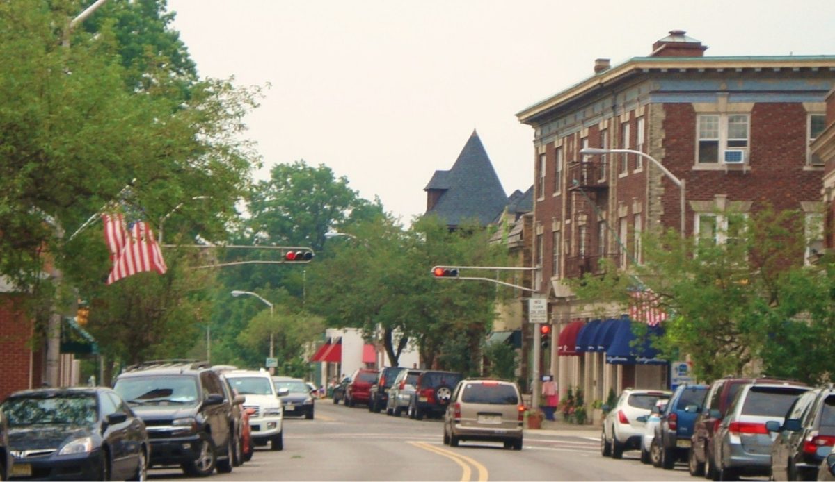 Street view in Upper Montclair, New Jersey, with trees, cars, and American flags  