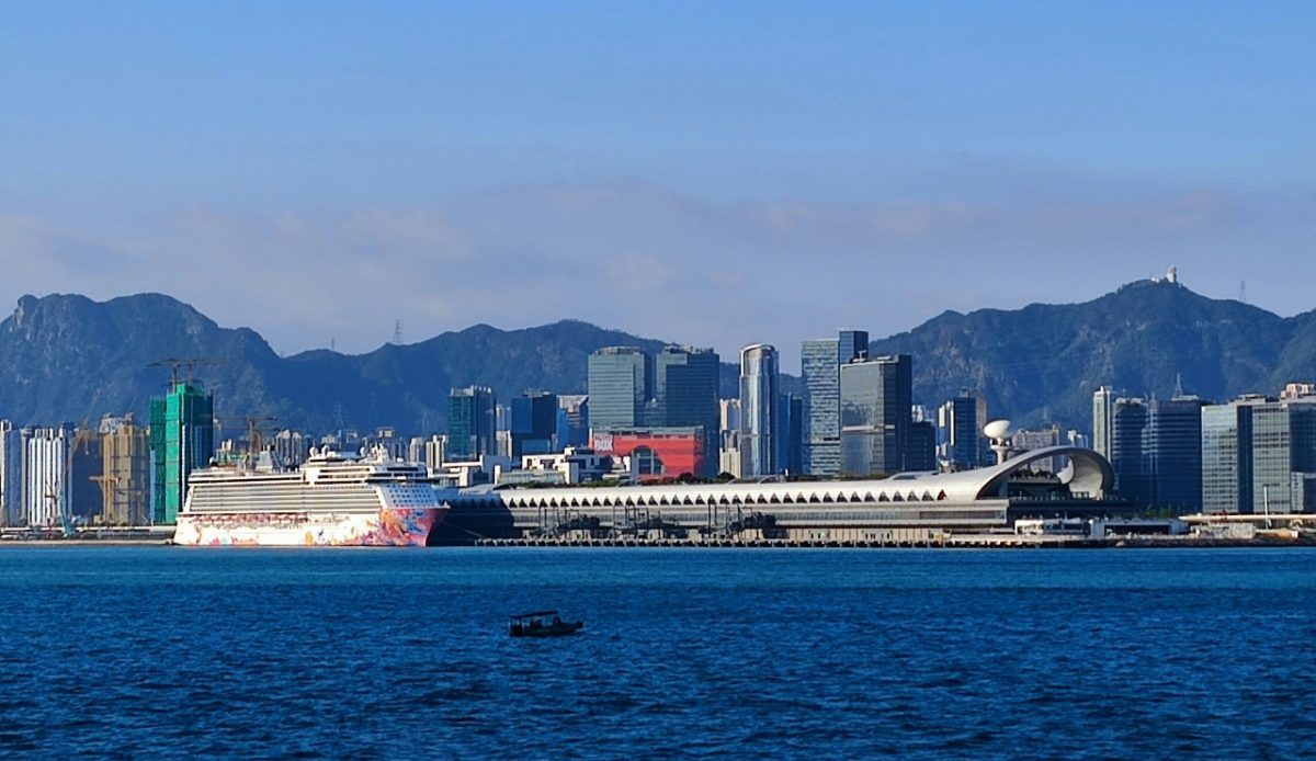 A cruise ship docked at the terminal in Hong Kong with city skyline in the background 