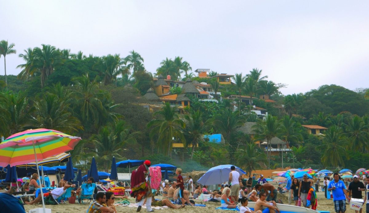 Sayulita, Nayarit Beachgoers enjoying the sun with colorful umbrellas and palm trees By 