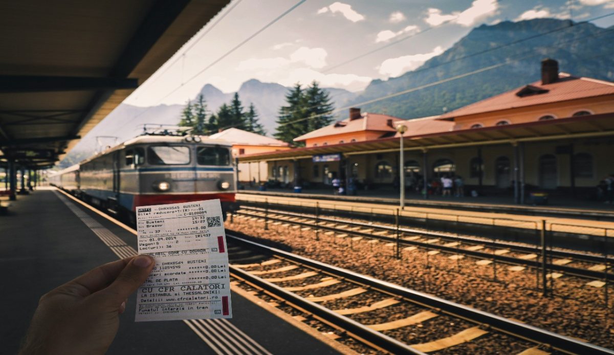 A person holding train ticket at a railway station with a train arriving in the background 