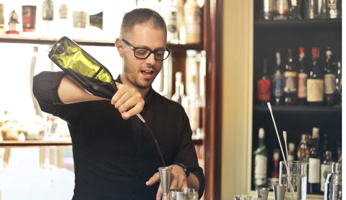 Bartender pouring drink into jigger at a bar counter