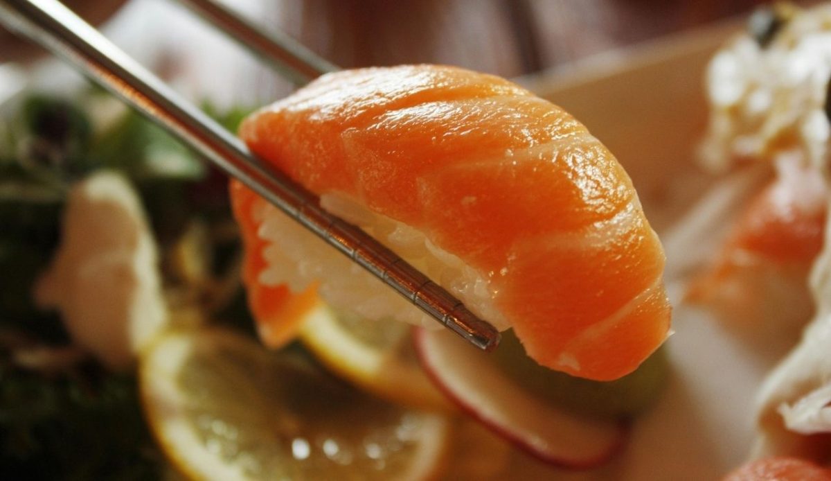 8 Airport Foods Every Traveler Should Avoid and Why 5 Chopsticks holding a piece of salmon sushi above a plate with lemon slices