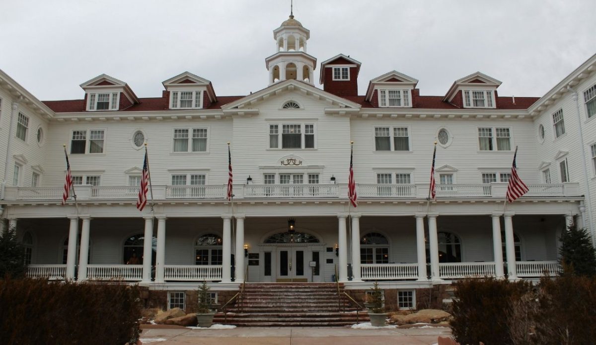 13 Haunted Places in the US Where You Can Spend the Night 1 Front entrance of the Stanley Hotel with white columns and American flags, Estes Park, Colorado, USA