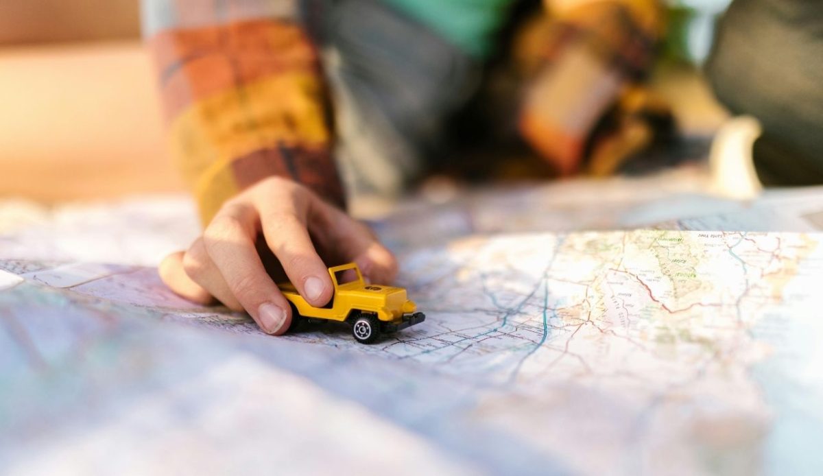 10 Reasons Travelers Sometimes Cancel Their Cruise Plans 9 Hand holding toy car over road map during travel planning