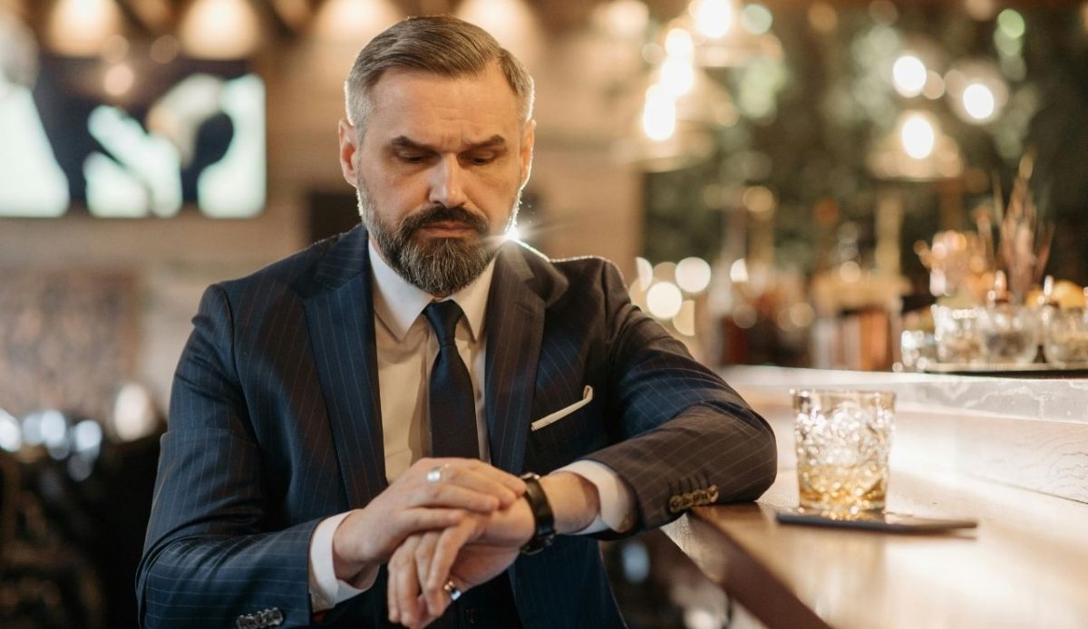 Man in a navy suit checking his watch at a bar 