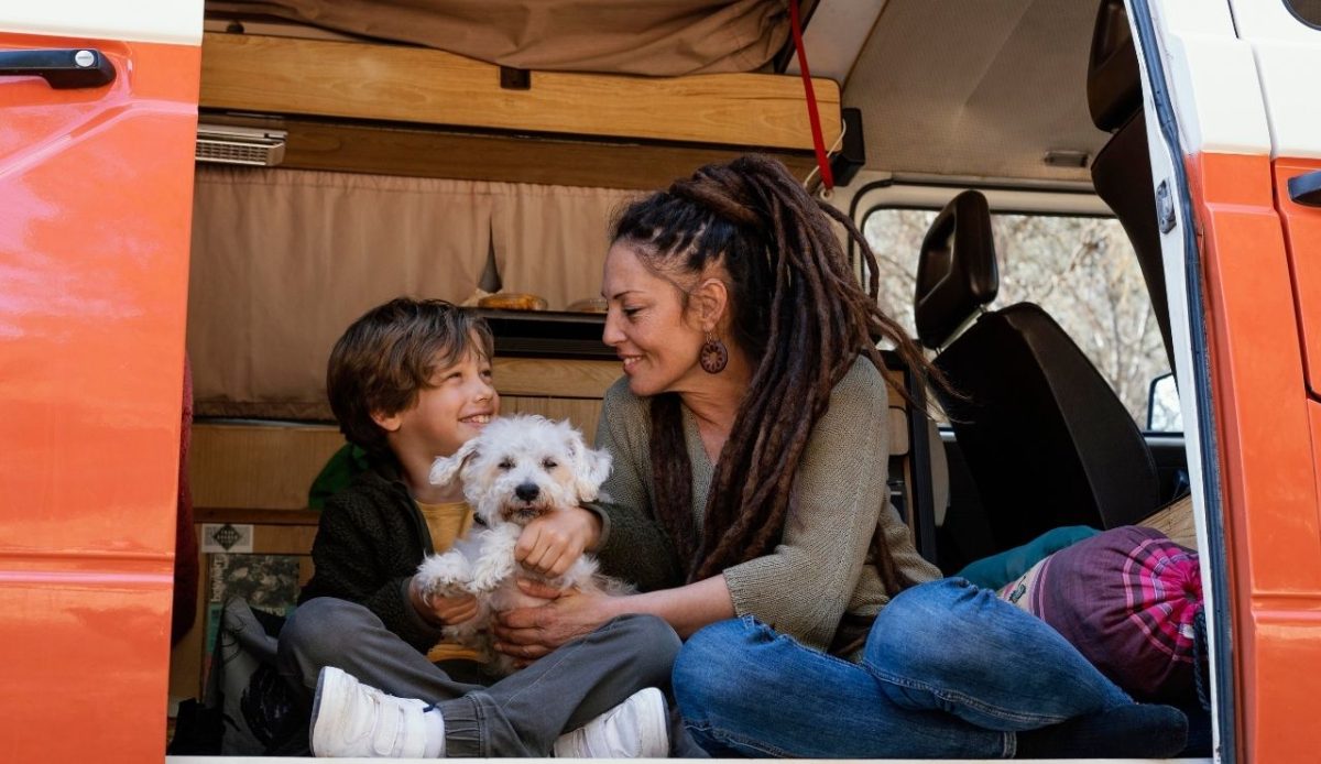 9 Reasons RVs Are Becoming America’s New Vacation Homes 2 Mother and son sitting in a camper van doorway playing with their white dog