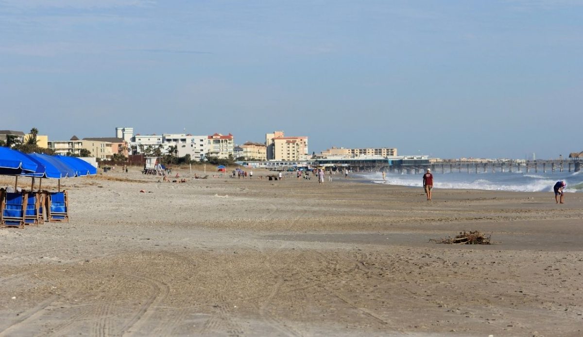 8 Famous East Coast Boardwalks and Beach Towns That Never Get Old 8 People walking along sandy shoreline near Cocoa Beach Pier, Florida, USA