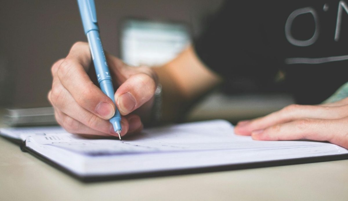 Person Holding Blue Ballpoint Pen Writing in Notebook     