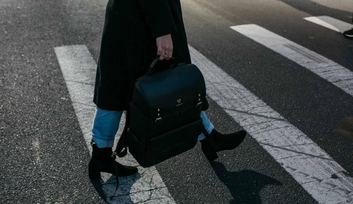 Person crossing street carrying a black backpack  