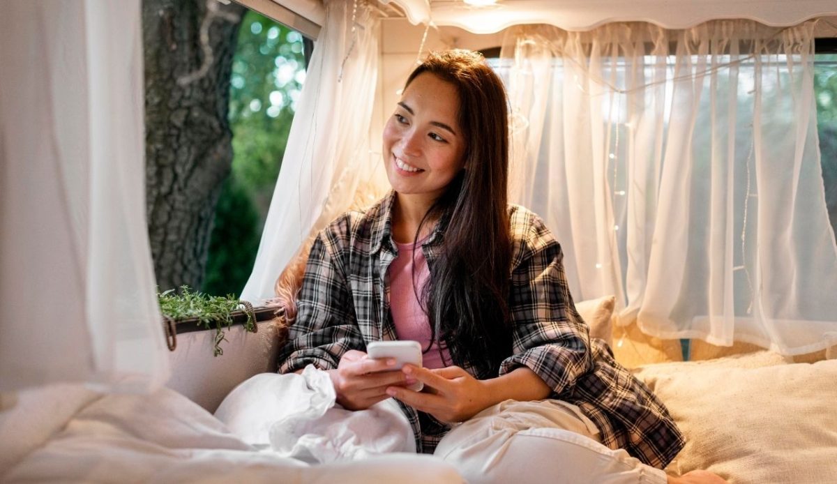 9 Reasons RVs Are Becoming America’s New Vacation Homes 7 Woman sitting inside a camper van holding a smartphone near a forest campsite