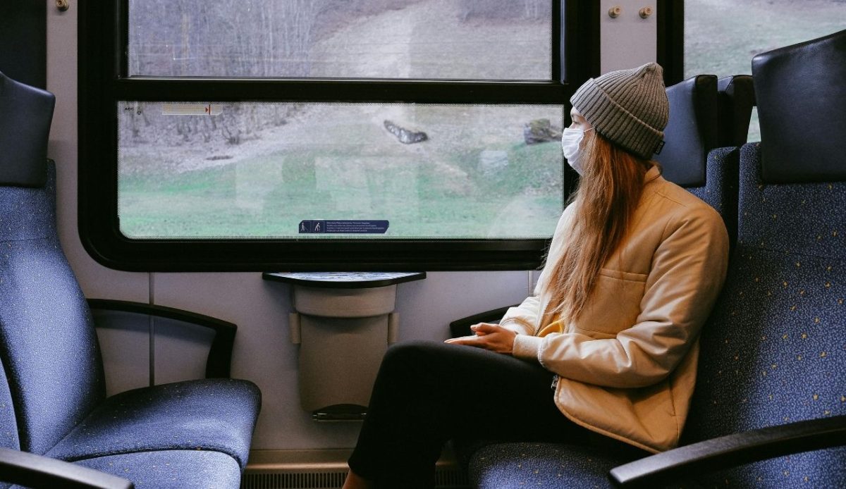 Woman wearing a face mask and beanie looking out the window while traveling on a train