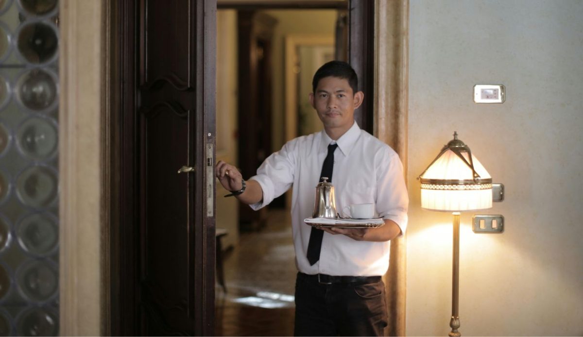 Waiter holding tray with coffee pot and cup near a doorway