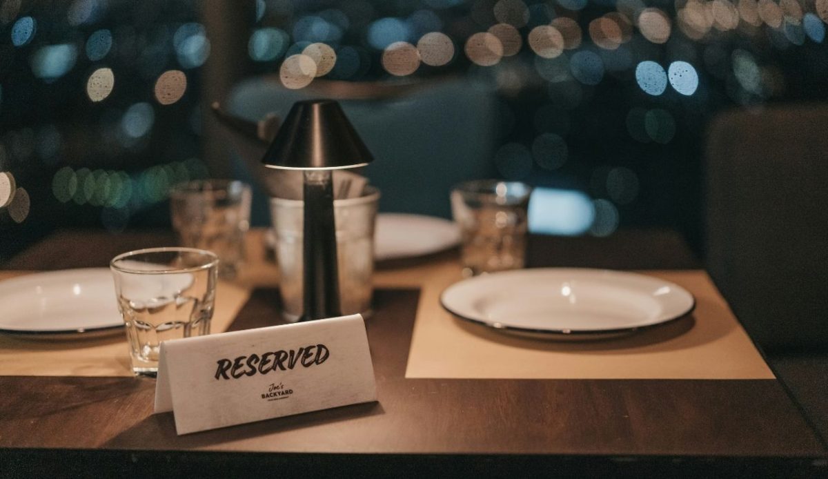 Reserved dinner table with plates and lamp at a waterfront restaurant, night view