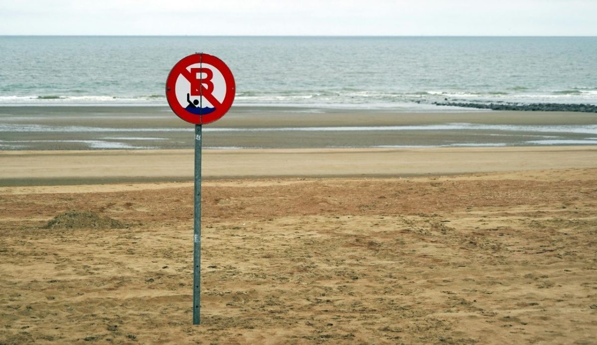 no swimming warning sign on empty beach near the sea