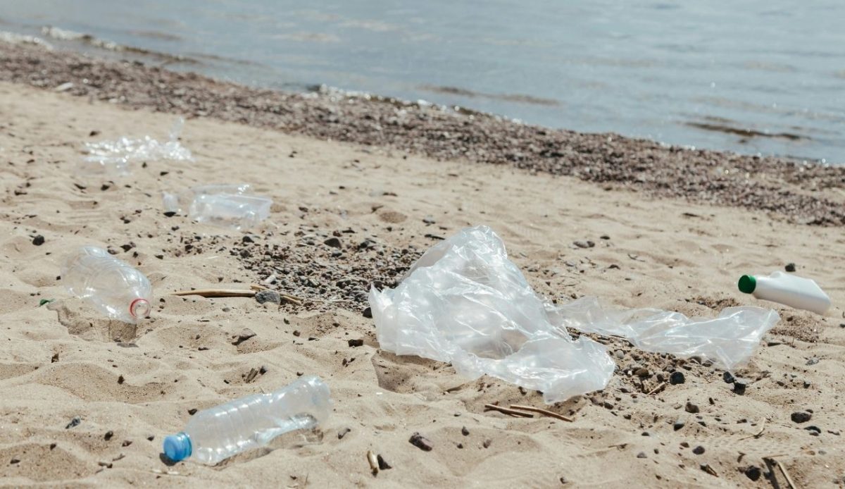 plastic bottles and trash scattered on sandy beach near water
