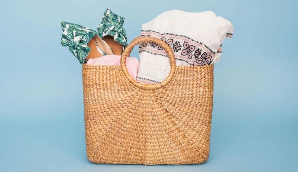 woven straw beach bag with summer clothes against blue background