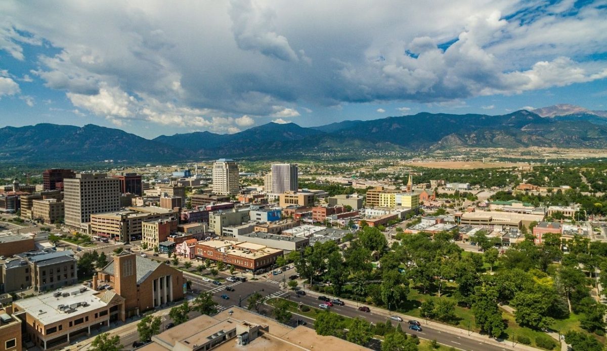 An aerial view of downtown Colorado Springs, overlooking Acacia Park at the intersection of Nevada Ave. and E Bijou St. with Pikes Peak in the distance                        