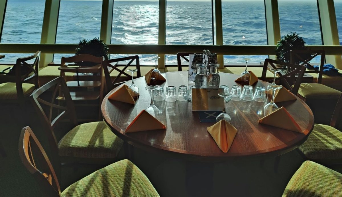 Cruise ship dining room table set with glasses and napkins facing the ocean                