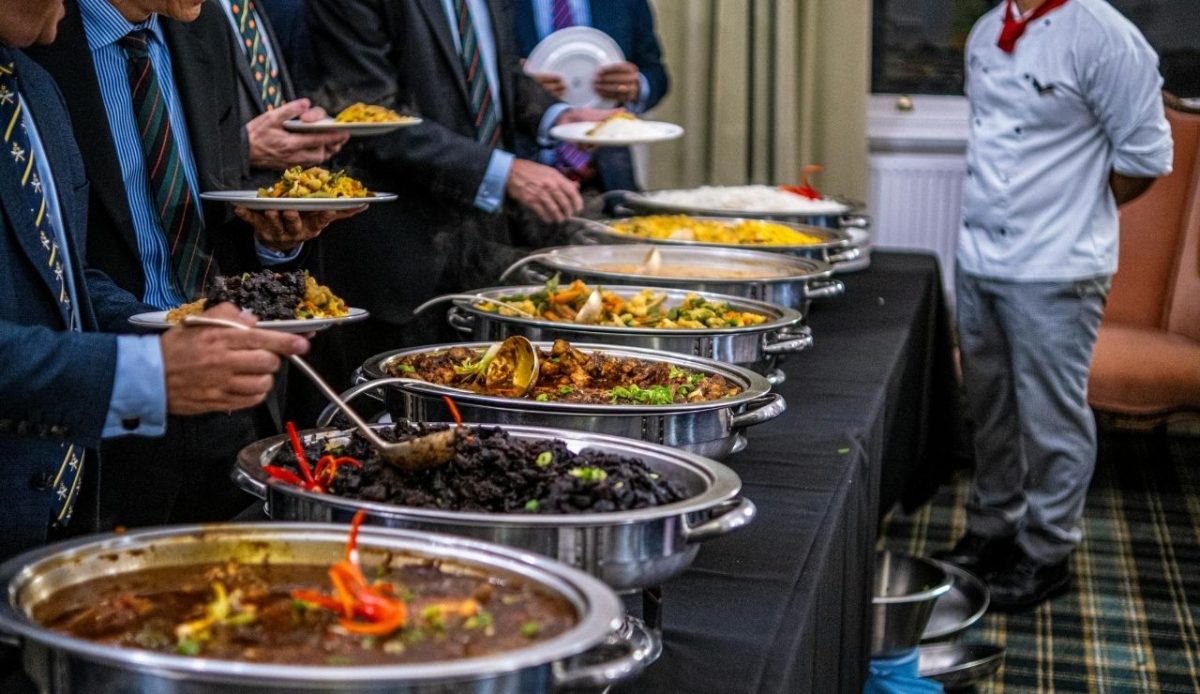 Guests lining up at a buffet table with multiple trays of food, filling their plates with a wide variety of dishes
