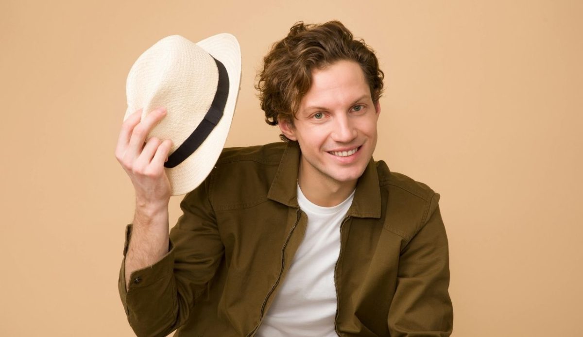 Man Wearing Brown Dress Shirt Holding White Fedora Hat expressing thankyou           