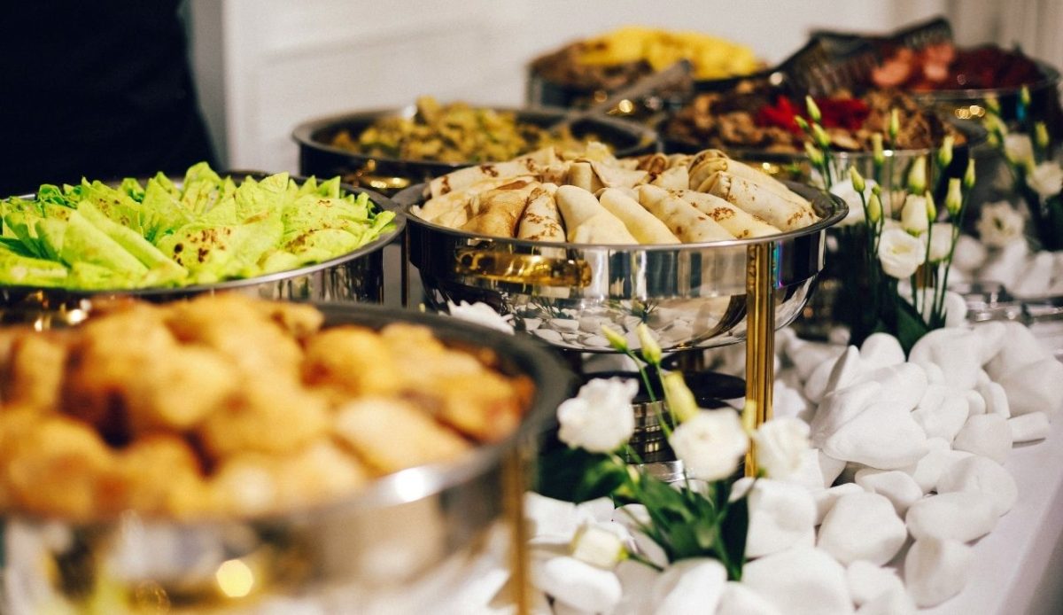 Open buffet chafing dishes displaying various foods in stainless-steel warmers